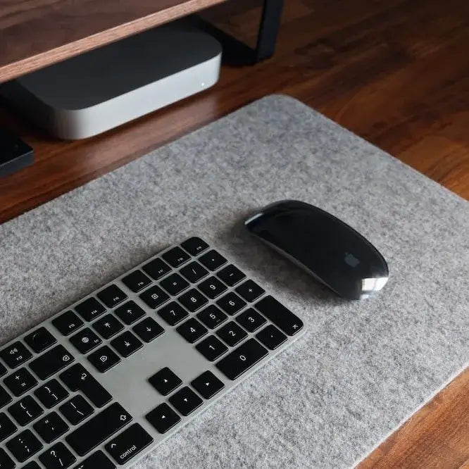 Detailansicht einer grauen Filz-Schreibtischunterlage auf einem Holztisch mit einer Tastatur und Maus, die eine ordentliche und minimalistische Arbeitsumgebung zeigt